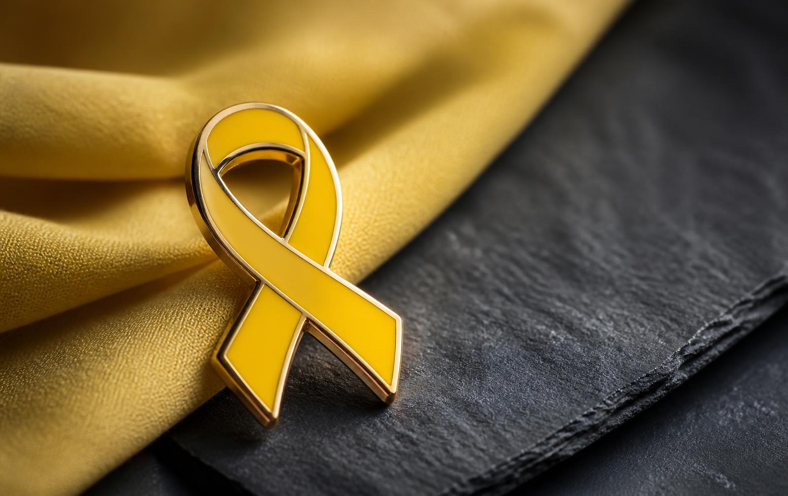 Pin metálico em formato de laço amarelo com acabamento dourado sobre tecido amarelo